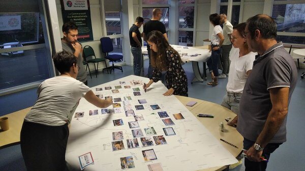 Photo de personnes autour de tables en train de positionner des cartes du jeu la fresque du climat